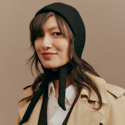 Woman wearing a black bonnet and beige coat against a brown background