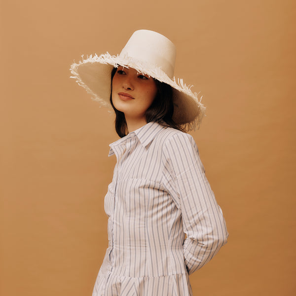 Woman wearing a white sun hat and striped shirt against a brown background