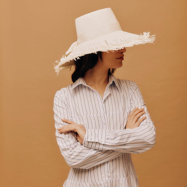 Woman wearing a wide-brimmed white hat against a brown background