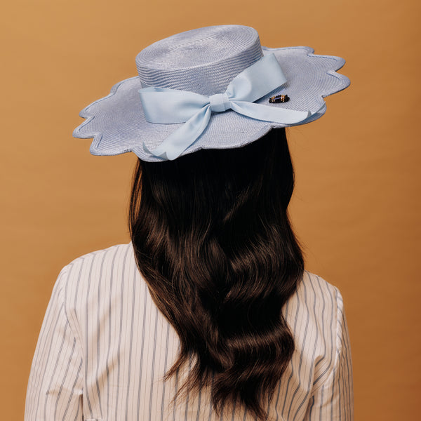 Woman wearing a light blue hat with a large bow on a brown background