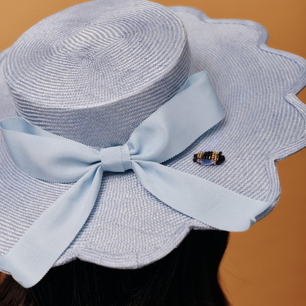 Light blue straw hat with a large bow on a brown background