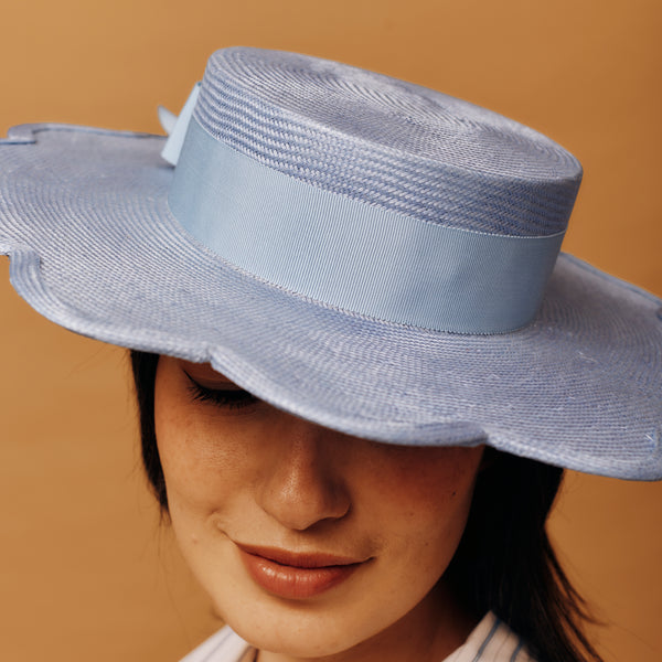 Woman wearing a light blue straw hat against a beige background