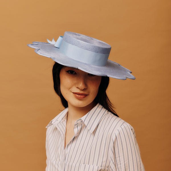 Woman wearing a light blue hat with a bow against a brown background