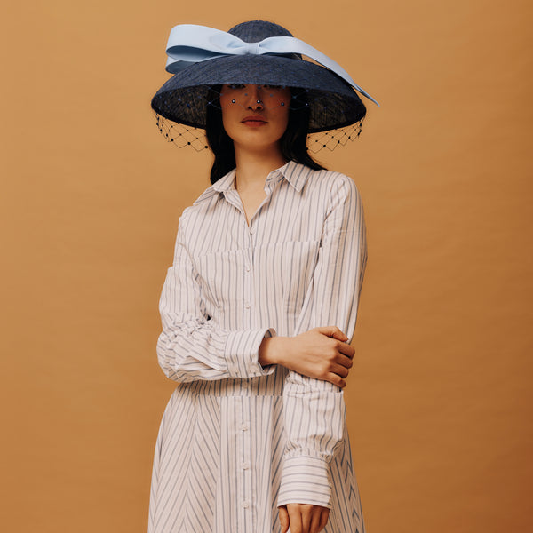 Woman wearing a large black hat with a blue ribbon against a brown background