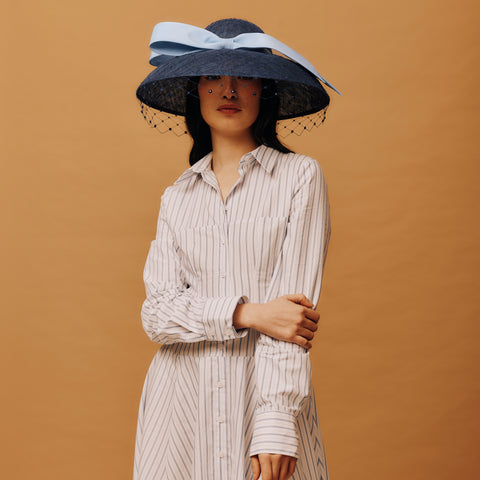 Woman wearing a large black hat with a blue ribbon against a brown background