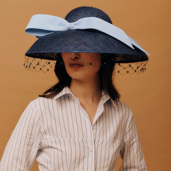 Woman wearing a large black hat with a light blue bow against a brown background