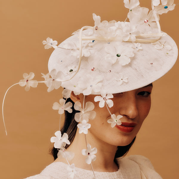 Woman wearing a white floral hat against a beige background