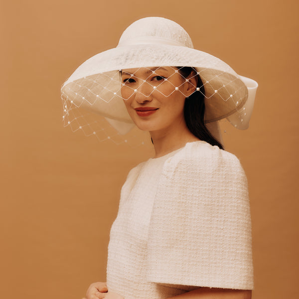 Woman wearing a white hat with a veil against a beige background