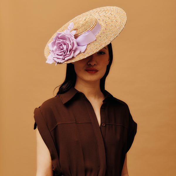 Woman wearing a straw hat with a pink flower against a brown background