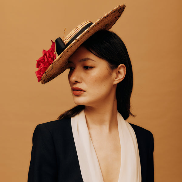 Woman wearing a straw hat with a red flower against a beige background