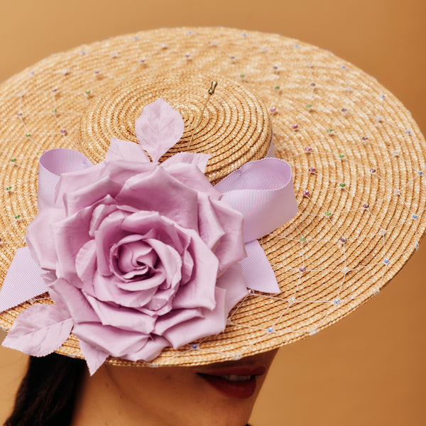 Straw hat with a large lilac flower and pink ribbon on a brown background