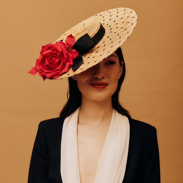 Woman wearing a straw hat with red flowers and a black ribbon on a brown background