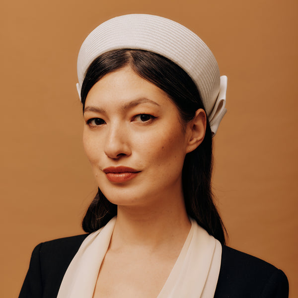 Woman wearing a white pill box hat with a bow on a brown background
