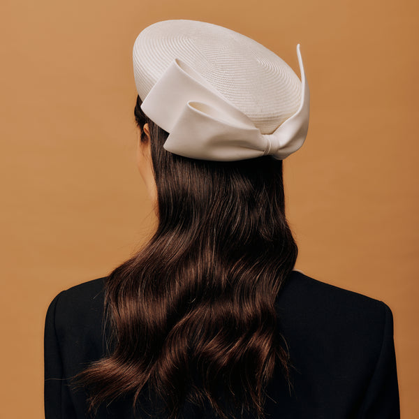 Person wearing a white pill box hat against a brown background