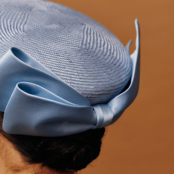 Blue pill box straw hat with a large bow on a brown background