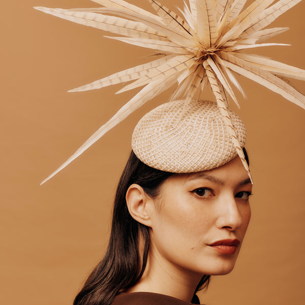 Woman wearing a decorative hat with a large feather on a brown background