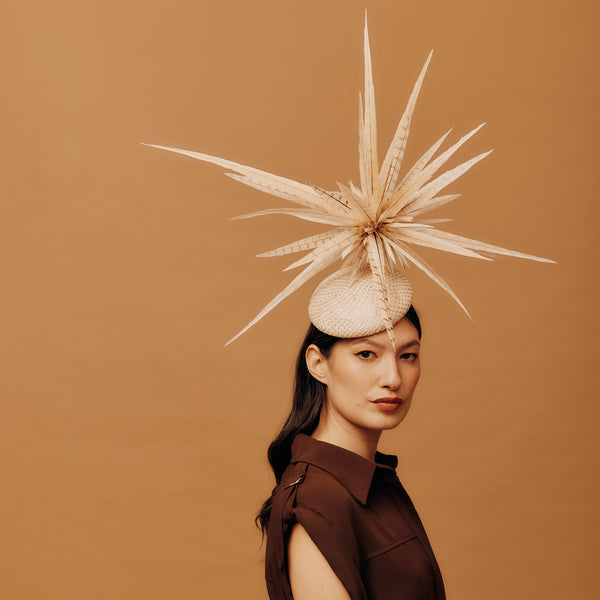 Woman wearing a decorative hat with a large feather on a brown background