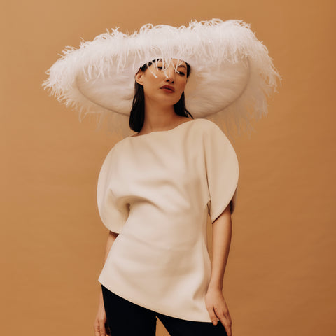 Woman wearing a large white feathered hat against a brown background