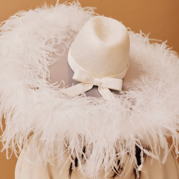 White straw hat with a bow on a feathered stand against a beige background