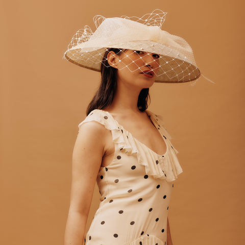 Woman wearing a large white hat with a veil against a brown background