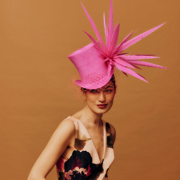 Woman wearing a vibrant pink hat with feather-like decorations against a brown background