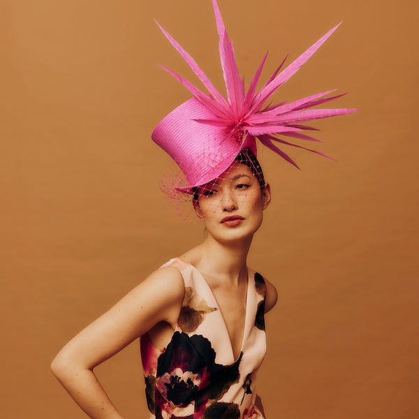 Model wearing a vibrant pink hat with feather-like decorations against a brown background