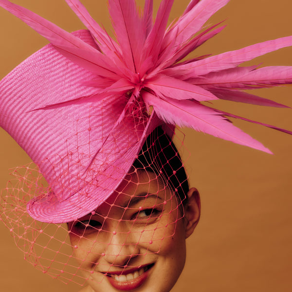 Woman wearing a pink top hat with feathers against a brown background