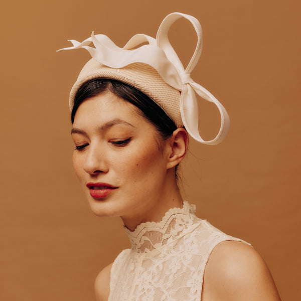 Woman wearing a straw headband with ivory bow against a brown background