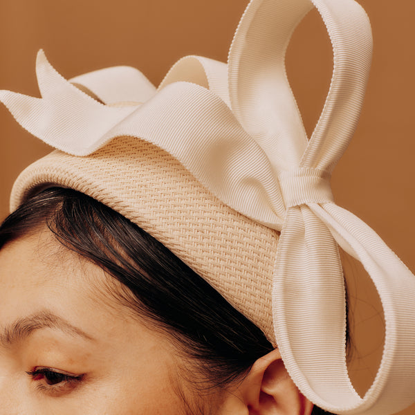 Beige hat with a large bow worn by a person against a brown background