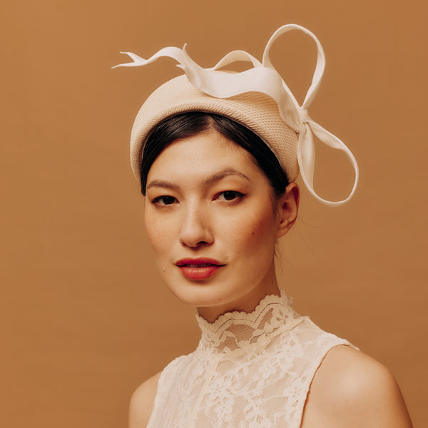 Woman wearing a beige straw hat with a bow against a brown background