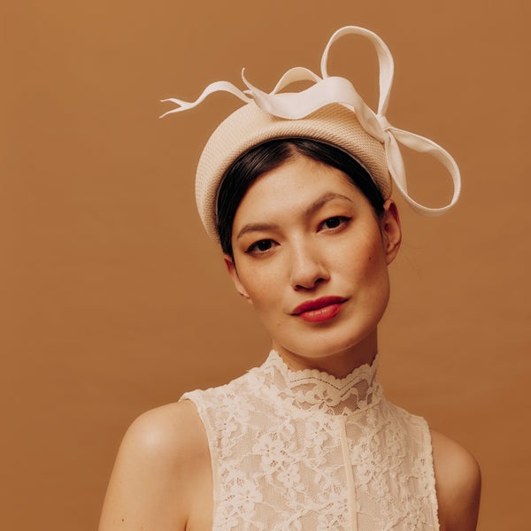 Woman wearing a beige straw hat with a bow against a brown background