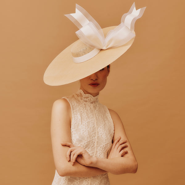 Woman wearing a large decorative hat against a beige background