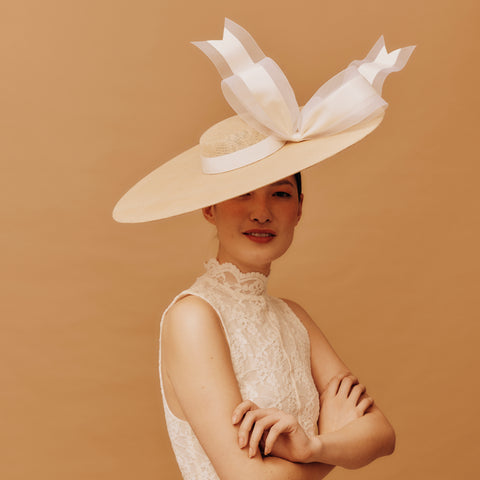 Woman wearing a large white hat with a bow against a beige background