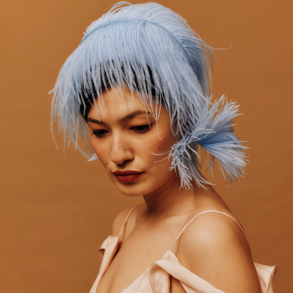 Woman with blue feather headband against a brown background
