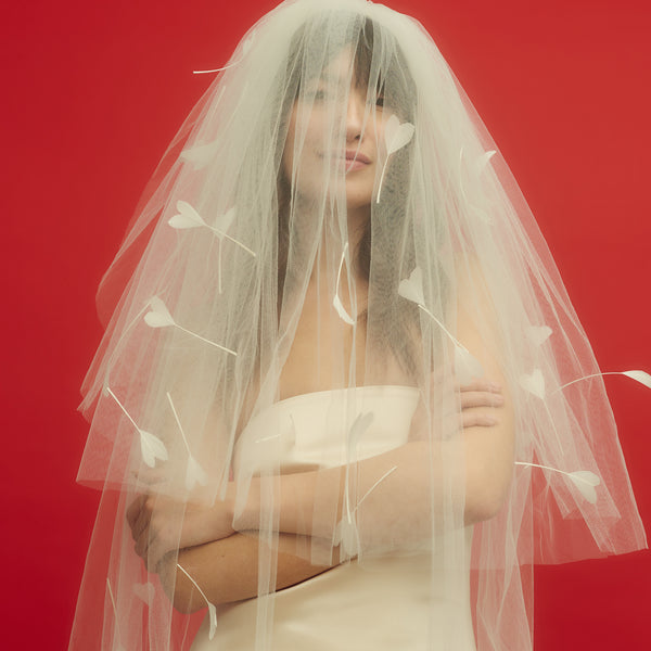 Awon Golding floor-length ivory white tulle veil with hand-cut heart shaped goose feathers. Blusher veil covering model's face