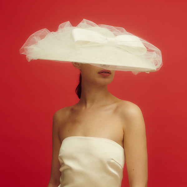Awon Golding wide brim bridal hat with tulle veil and duchess satin bow. The veil flips up for the bride's reveal